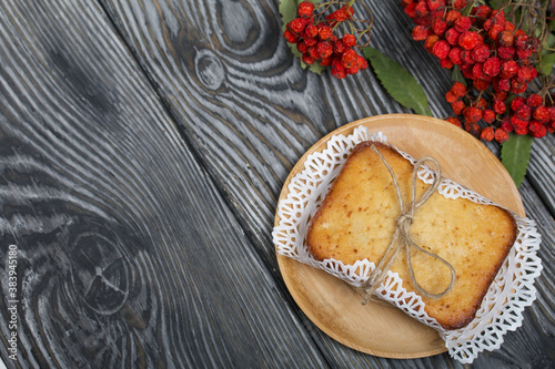 Freshly baked cupcake on a napkin. Tied with twine. Nearby is a dried rowan branch with red berries. Against the background of black pine boards.