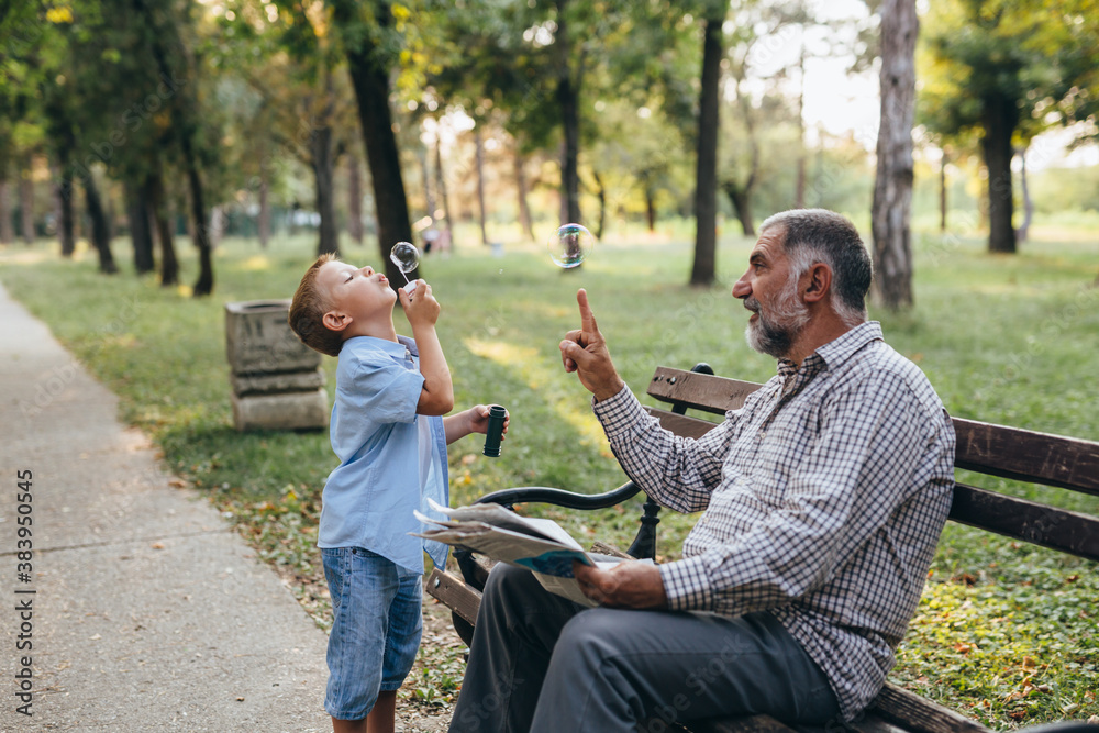 Obraz premium grandfather and grandson sitting on the bench in park