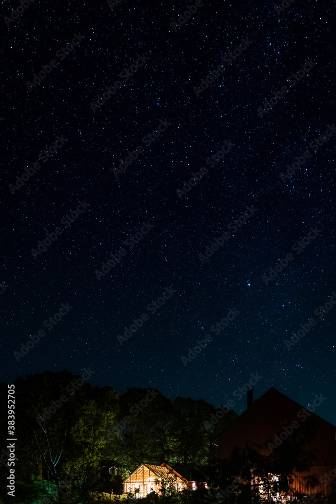 night sky with stars over an illuminated greenhouse in the swedish countryside