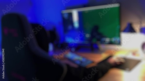 Teenage PC Gamer Playing First-Person Shooter in Subdued Light. A teenage gamer dressed in a black hoodie plays a multiplayer first-person violent shooter video game on a PC.