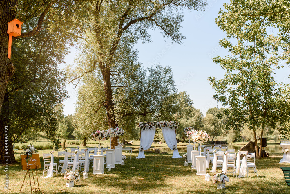 Wedding ceremony outdoors in the park. White chairs decorated with roses. Wedding ceremony outdoors in the park. White chairs decorated with roses.