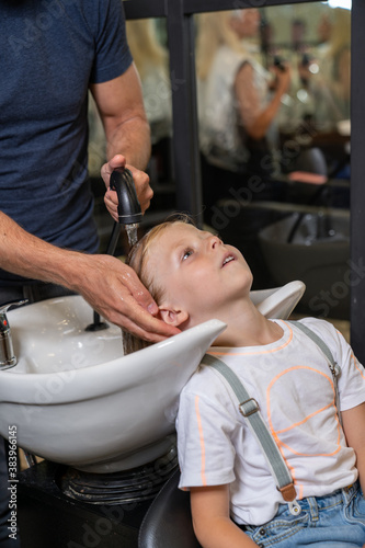 a blonde boy gets his hair washed in a barber shop before cutting his hair.