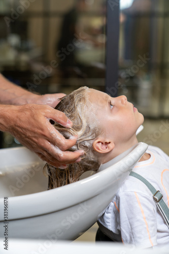 a blonde boy gets his hair washed in a barber shop before cutting his hair.