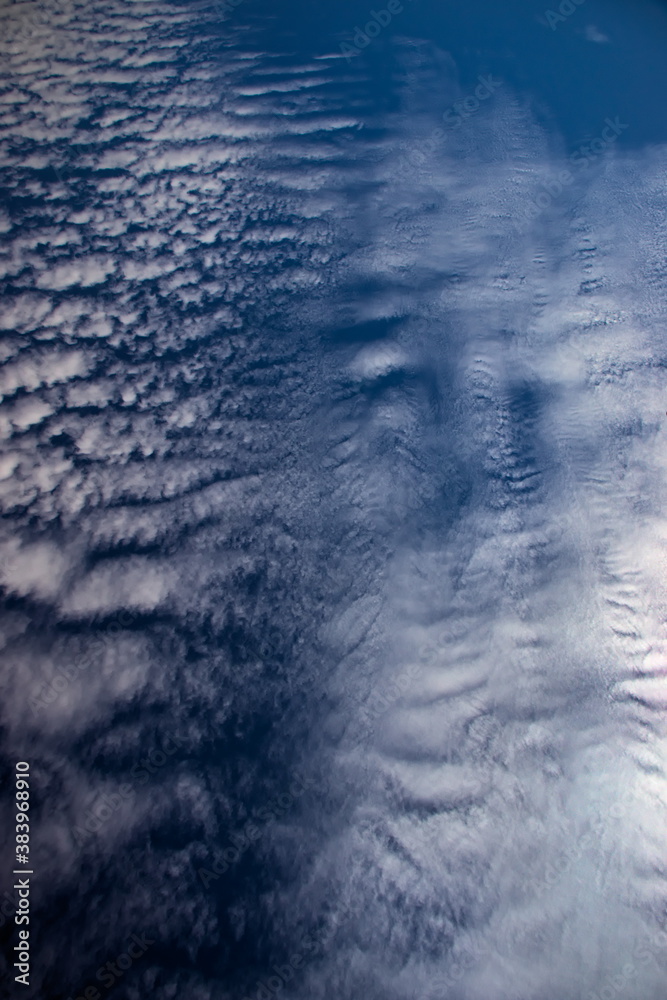 vein of Cirrocumulus clouds, partially covering the sun, blown by the winds under a navy blue sky.