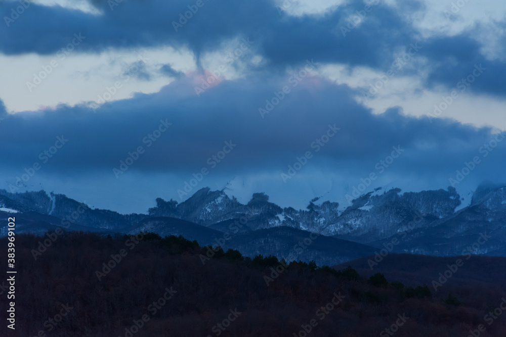 Panorama of snowy mountains at sunset. Majestic clouds over the mountains. Blue winter background. The beautiful landscape of the Crimean mountains. Calm, balanced background. January frosts.