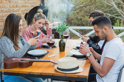 Urban millennial people using smart phones. Serious guy watching news on mobile smartphone. Young friends sitting at a bar table