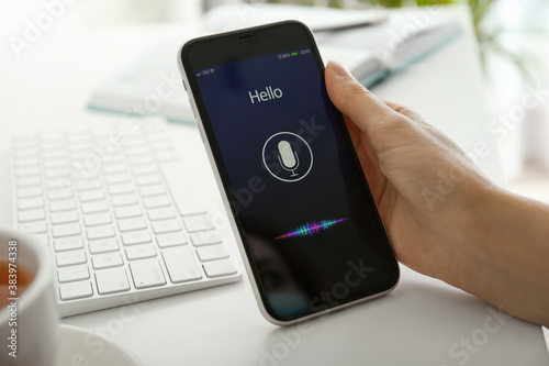 Woman using voice search on smartphone at white table, closeup