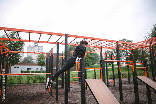 Young woman do the workout plays sports in the park outside playground
