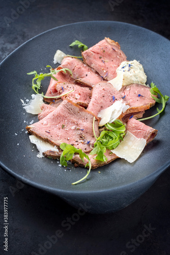 Modern Style traditioneller Beefsteak Aufschnitt mit Rucola Salat und Parmesan Käse angeboten als Draufsicht auf einem Modern Design Teller