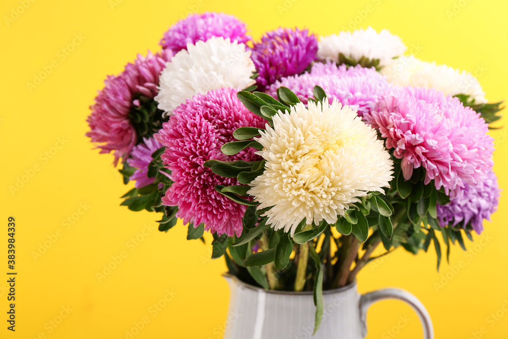 Beautiful asters in jug on yellow background, closeup. Autumn flowers