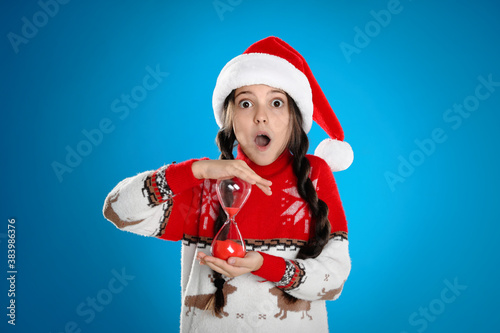 Girl in Santa hat with hourglass on light blue background. Christmas countdown © New Africa