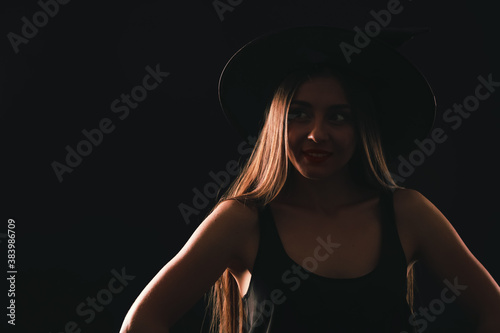Young woman wearing witch costume on black background, space for text. Halloween party © New Africa