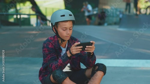 Busy teenager pracing race game online video entertaining on mobile phone in skatepark. Modern kids. Urban lifestyle. Skateboarding. Technology. Outdoors. photo