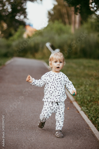 boy walking in a beautiful white suit against the background of nature, baby about one year old learning and playing outdoors. © Aleksei Zakharov