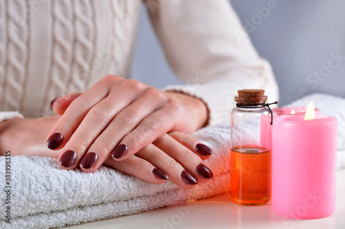 Close up of woman hands with brown nails polish color on a towel in a beauty salon on a white desk with decoration. Manicure and beauty concept