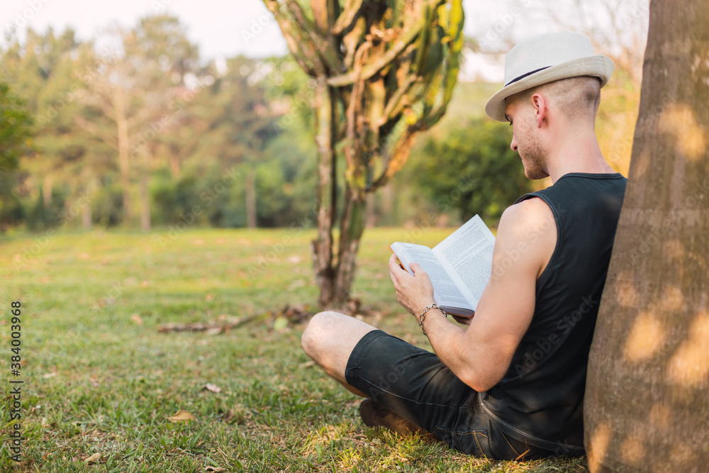 Man lying in a tree reads a book. Tourist with hat, reads a book in the park. Man reads a book. Relaxation and outdoor concept.