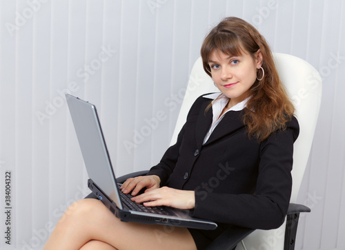 Beautiful young girl sits in office armchair with laptop