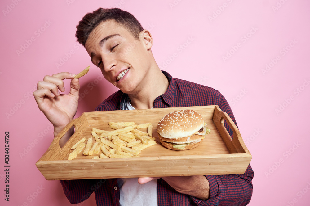 Man with fast food eating hamburger french fries pink background Man with fast food eating hamburger french fries pink background