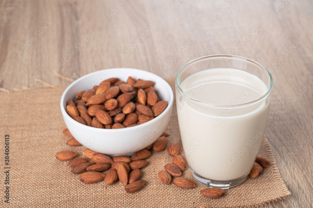 Glass of almond milk with almond in white bowl on table. Glass of almond milk with almond in white bowl on table.