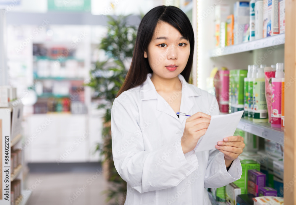 Chinese female pharmacist is checking medicine with notebook in drugstore