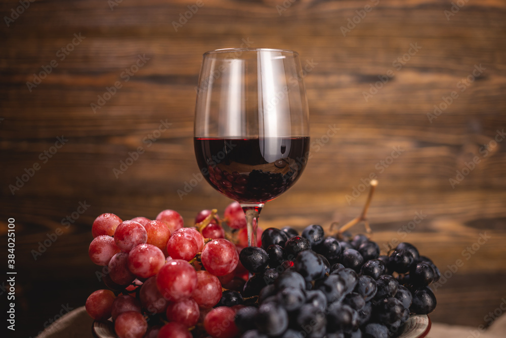 Bottle of dry red wine with a glass and a bunch of grapes on a wooden table. Concept of viticulture and winemaking