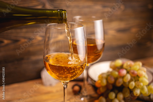 Bottle of dry white wine with a glass and a bunch of grapes on a wooden table. Concept of viticulture and winemaking