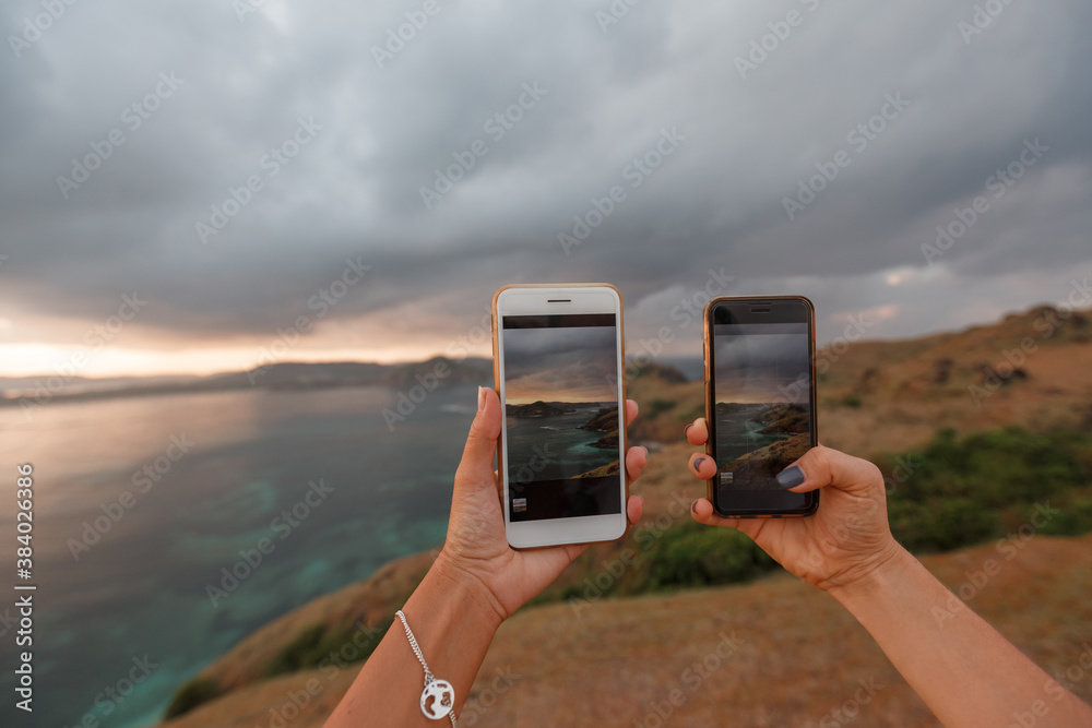 Two women tourist taking photo on sea beach with mobile smart phone camera at sunset, hands close up. Meresse hill Lombok Indonesia Two women tourist taking photo on sea beach with mobile smart phone camera at sunset, hands close up. Meresse hill Lombok Indonesia