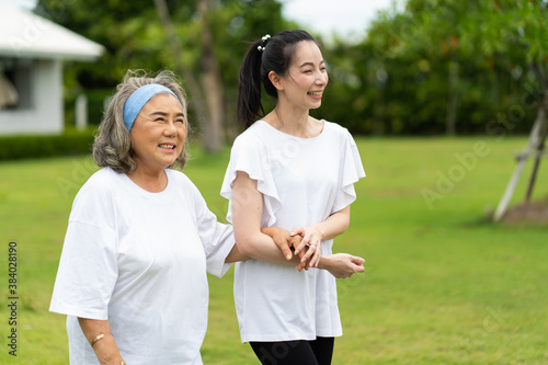 Asian senior mother and adult daughter holding hands and exercise walking outdoor at park.