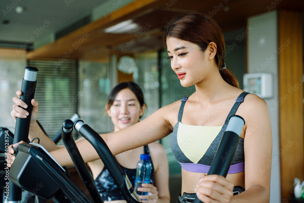 Fototapeta premium Beautiful woman work out on machine with trainer at gym.