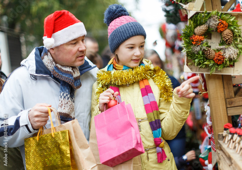 Cheerful preteen girl with father shopping decorations on Christmas market..
