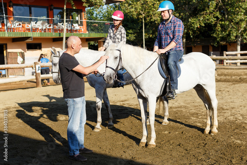 Portrait of woman and man with trainer riding horse at farm at summer day