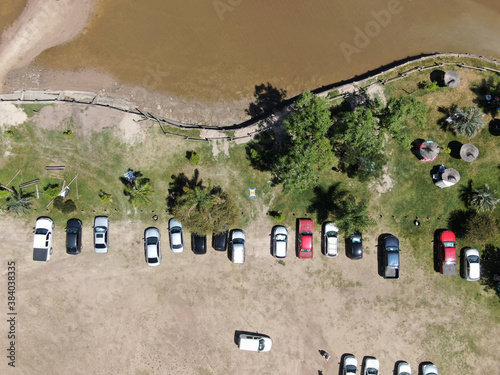 Foto aérea, con vista cenital de la costa de un río y autos estacionados.  photo