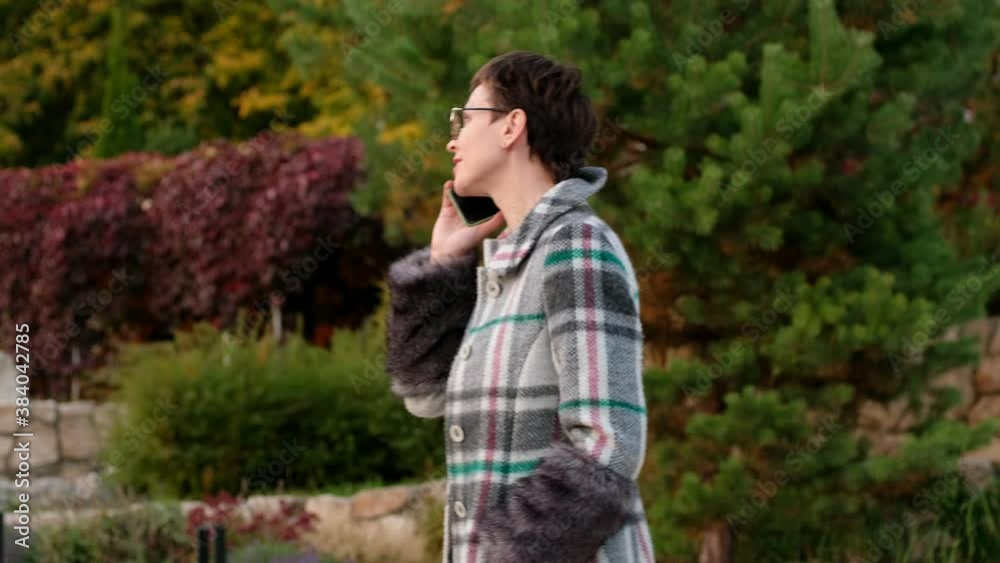 Beautiful business woman in glasses talking on phone in park. Realtor is negotiating purchase of real estate. Beautiful business woman in glasses talking on phone in park. Realtor is negotiating purchase of real estate.