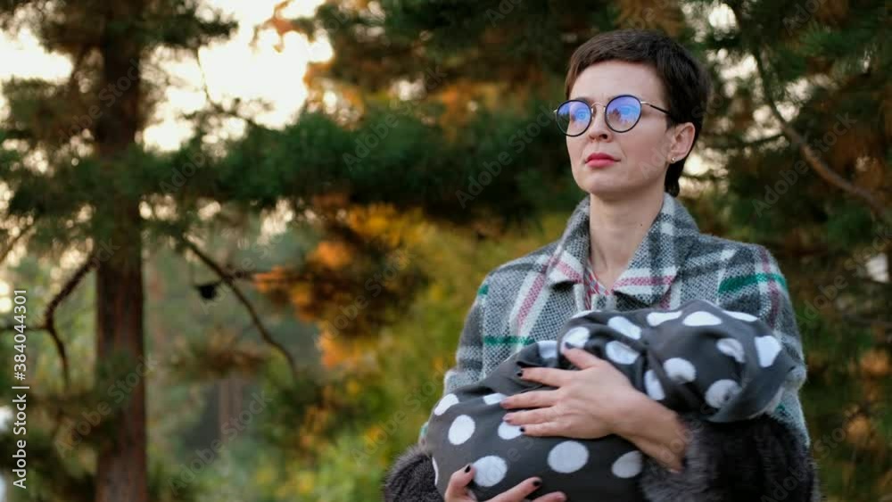 Beautiful woman in glasses cradles a baby in her arms in park. Beautiful woman in glasses cradles a baby in her arms in park.