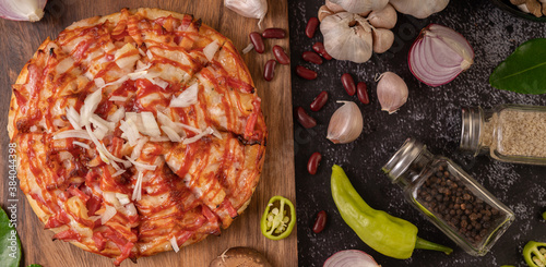 Fototapeta Naklejka Na Ścianę i Meble -  Pizza on a wooden tray with bell peppers, garlic, chili, shiitake mushrooms, and a jar of pepper seeds.