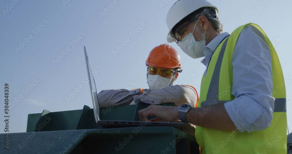 Engineers in masks using laptop on construction site Engineers in masks using laptop on construction site