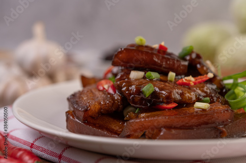 Sweet pork in a white plate sprinkled with chili and chopped scallions.