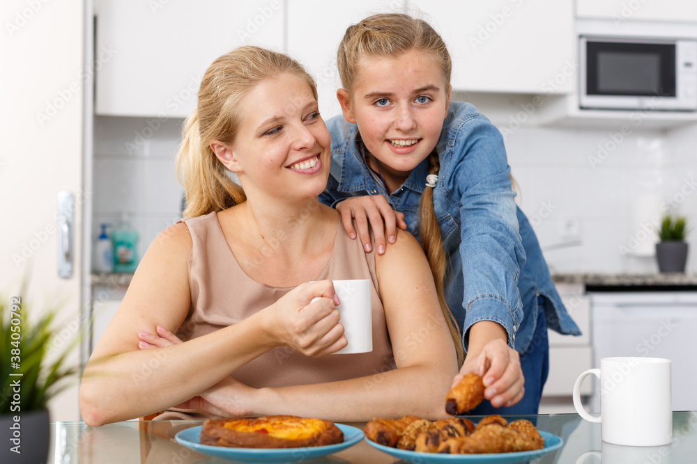Portrait of happy mother and teenage daughter drinking tea at kitchen