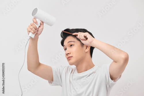 Young asian man holding hair dryer and comb creating new hairdo on white background