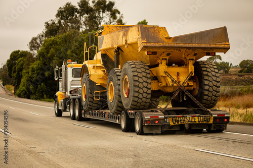 A very large haul dump truck being hauled by an 18 wheel truck down a freeway