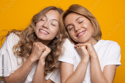 Delightful caucasian women with blonde hair gesturing happiness on a yellow wall in white t-shirts