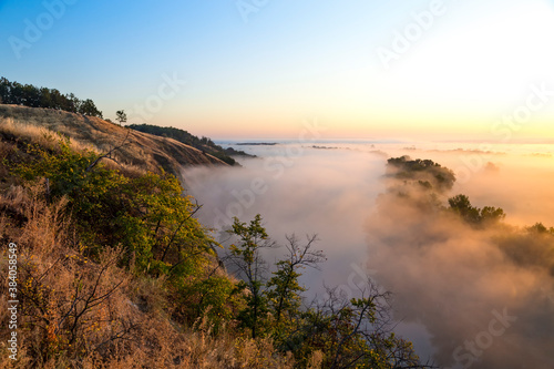 Beautiful panoramic landscape with river valley covered by thick fog in autumn in the early morning. Sunrise.