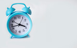 A blue alarm clock stands on a white background. Place for text