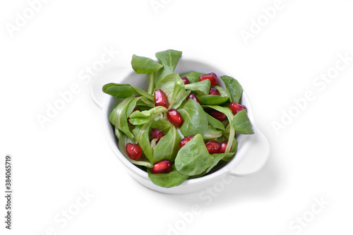 Pomegranate on green corn salad in white bowl on white background