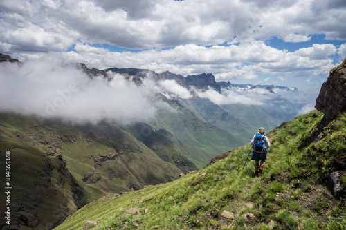 A hiker on a trail/ path high in the Drakensberg mountains with the spectacular range stretching away in the distance.