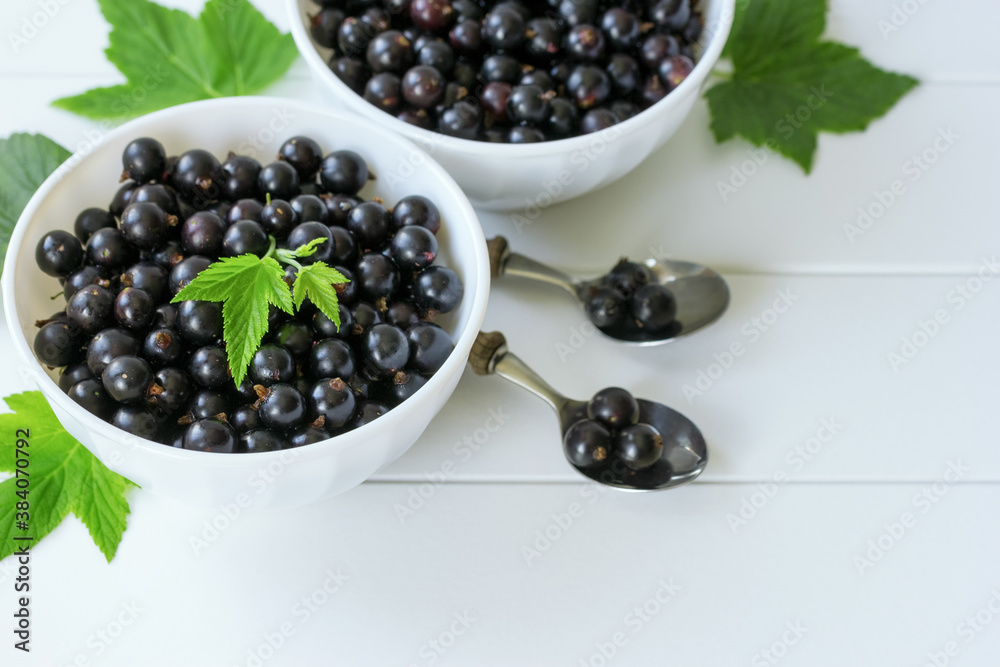black currant berries and green currant leaves on the table close-up. background from berries of black currant in white bowls view above. black currant berries and green currant leaves on the table close-up. background from berries of black currant in white bowls view above.