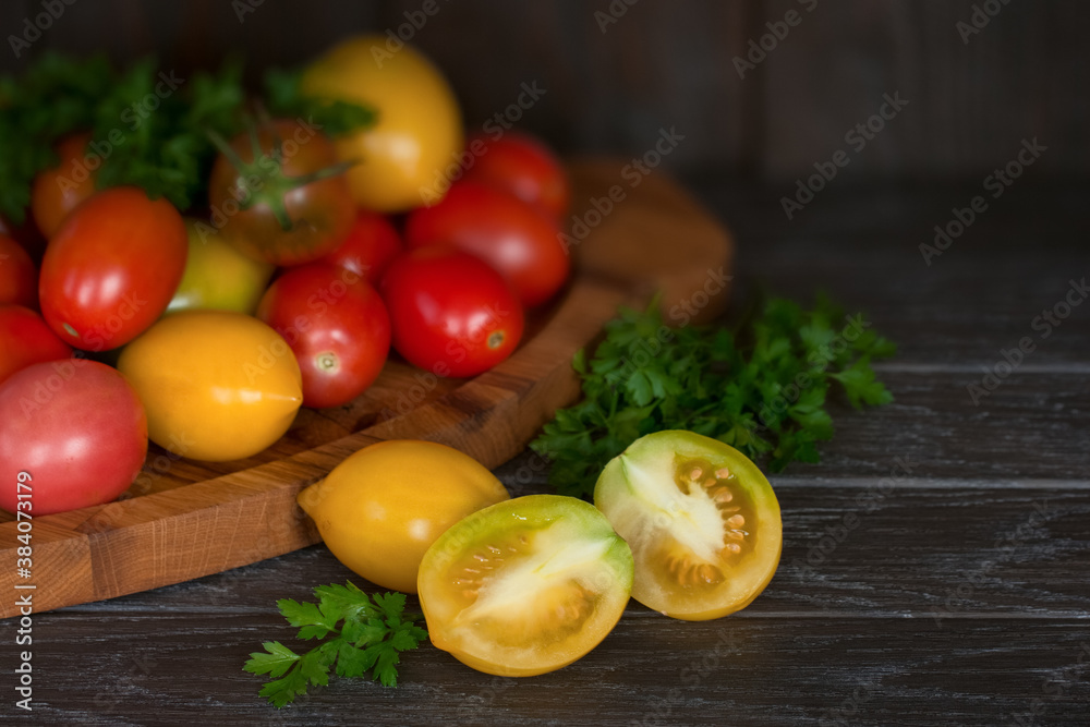 fresh tomatoes and sprigs of parsley on the table close-up. background with red and yellow tomatoes in a wooden box. fresh tomatoes and sprigs of parsley on the table close-up. background with red and yellow tomatoes in a wooden box.