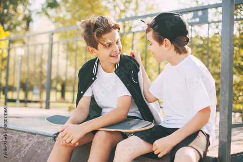 Two cute teenagers sit in a skatepark, relax after skateboarding and chat. Boys enjoy their free time in the skate Park, sitting on the ramp. The concept of youth, unity and friendship © Sviatlana