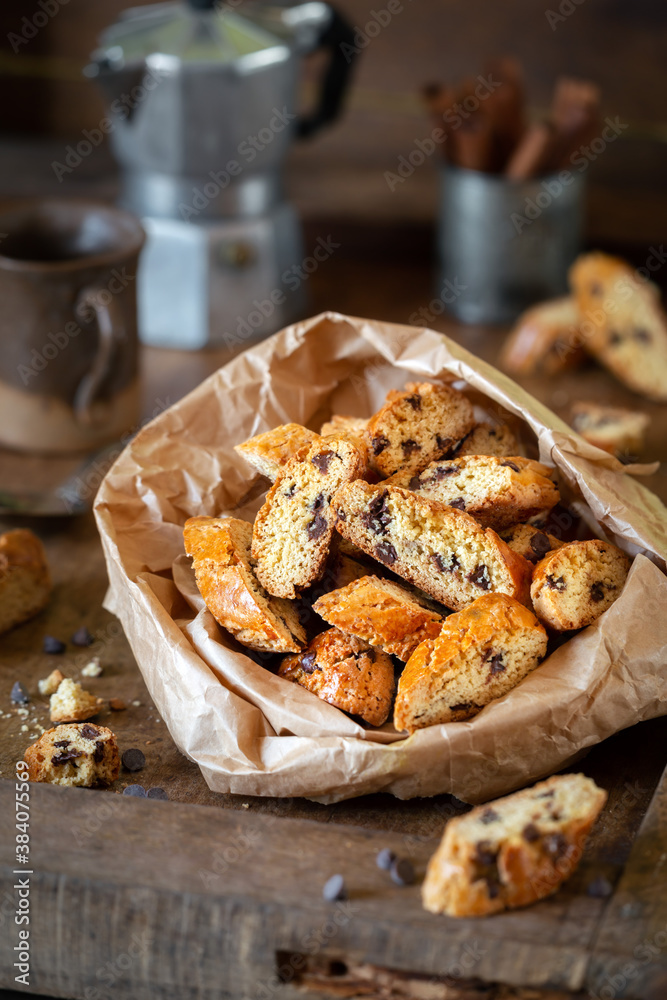 Delicious homemade cantucci biscuits or Italian biscotti with chocolate drops on dark rustic wooden table with a coffee pot and a cup at the background