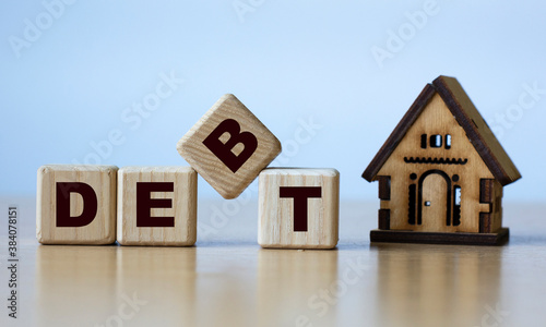 DEBT word on cubes on a light background with a wooden house